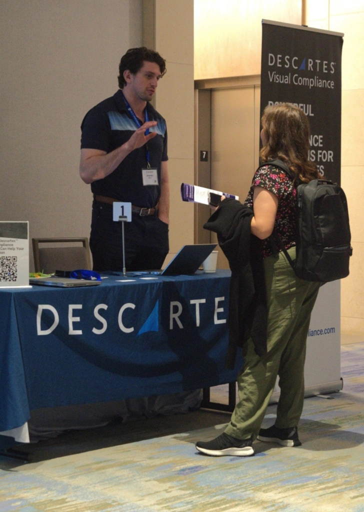 A member of the university export compliance community standing at Descartes’ AUECO booth, in discussion with Graeden Bird on how Descartes export compliance solutions can help.